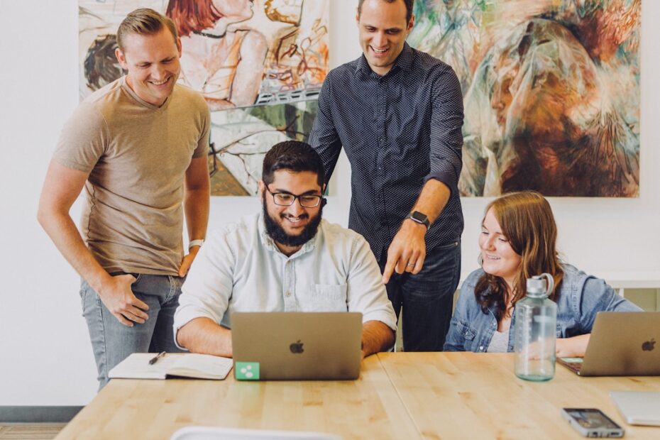 Four individuals collaborate on laptops, discussing AI management strategies in a bright, modern workspace.